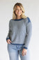 A woman wearing a navy and white striped knit sweater with blue jeans, standing against a light gray studio background.