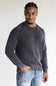 A man wearing a dark gray ribbed knit crewneck sweater and light blue jeans, standing against a plain light gray background.