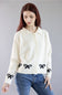 A woman wearing a cream-colored knit cardigan with black bow details on the front and cuffs, paired with blue jeans, against a solid gray studio background.