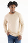 A man wearing a light beige knit crewneck sweater with raglan sleeves and blue jeans, standing against a plain white background.