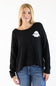 A woman wearing a black knit sweater with a white ghost graphic on the chest pocket, paired with blue jeans, against a plain white background.