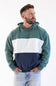 A man wearing a color-block hoodie with green, white, and navy blue sections, paired with light-wash jeans, photographed against a plain white background.