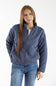 A woman modeling a slate blue quilted zip-up jacket with a stand collar, paired with blue jeans, against a plain white studio background.