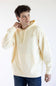 A man wearing a cream-colored hoodie with a small shield logo on the left chest