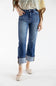 A model wearing a pair of medium-wash blue cropped jeans with rolled cuffs, paired with a patterned top and beige woven flats, shot against a plain white studio background.