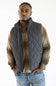 A man wearing a dark gray diamond-quilted zip-front vest over a brown and beige plaid button-up shirt, paired with blue jeans, against a plain white background.
