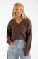 A woman with wavy blonde hair wearing a patterned headband, a dark brown V-neck button-down cardigan, and light-wash denim jeans.