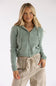 A woman modeling a sage green ribbed knit zip-up hoodie with drawstrings and front pockets, paired with beige drawstring pants, against a plain white studio background.