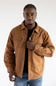 A man wearing a brown button-up overshirt jacket over a black t-shirt and blue jeans, photographed against a plain white studio background.