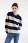 A woman wearing a navy blue and cream striped knit sweater with blue jeans, standing against a plain white studio background.