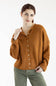 A woman wearing a long-sleeve knit cardigan in a warm rust-orange color with white buttons, paired with olive green pants, against a plain white background.