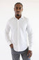 A man wearing a white long-sleeve button-down shirt and gray trousers, standing against a plain white studio background.