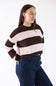 A woman wearing a brown and light pink striped knit sweater with dark blue jeans, photographed against a plain white studio background.