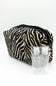 A zippered cosmetic pouch with a black and beige zebra print pattern, shown with two small clear plastic hand sanitizer bottles in front on a white background.