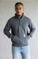 A man wearing a dark gray quarter-zip pullover sweatshirt with a small Carhartt logo patch on the front pocket, paired with light blue jeans, standing against a neutral gray background.