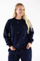A woman wearing a navy blue crewneck fleece sweatshirt with an all-over pink and white candy cane embroidery pattern, paired with matching navy sweatpants.