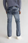 Rear view of a person wearing light blue denim jeans with a ribbed gray sweater and white sneakers, standing against a plain light gray studio background.
