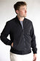 A man wearing a black zip-up bomber jacket over a gray t-shirt and off-white pants, standing against a plain light gray background.