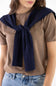 A woman wearing a brown short-sleeve knit top and blue jeans, with a navy blue cable-knit sweater draped over her shoulders and tied in a knot at the front.