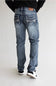 Rear view of a person wearing light blue denim jeans with decorative stitching on the back pockets, a black top, and black-and-white sneakers against a plain light gray studio background.