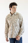 A man wearing a beige and light brown camouflage Carhartt long-sleeve button-up shirt with blue jeans, standing against a plain white background.