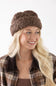 A smiling blonde woman wearing a brown chunky knit slouchy beanie and a brown plaid flannel shirt, photographed against a clean white background.