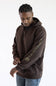 Three-quarter profile view of a male model against a white background, wearing a dark clove brown Carhartt hooded sweatshirt with "carhartt" printed down the left sleeve, paired with medium wash denim jeans.
