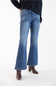 A model from the waist down wearing medium-dark wash blue flare jeans, a dark navy cardigan, and brown ankle boots, standing against a plain white studio background.