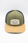 A two-tone trucker cap with an olive green front panel and brim, dark navy mesh back panels, and a tan snapback closure. The front features a cream-colored patch with the text 'MARSH WEAR 2010'.