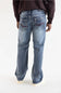 Rear view of a person wearing light-wash blue jeans with a dark brown sweatshirt and white sneakers against a plain white studio background.