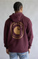 A person shown from the back wearing a maroon hooded sweatshirt with a large gold Carhartt logo graphic on the back, paired with blue jeans against a plain gray studio background.