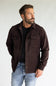 A man wearing a dark brown corduroy button-up shirt jacket over a black t-shirt and blue jeans, standing against a light gray studio background.