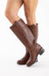 A pair of knee-high brown leather boots with a low block heel, shown on a model's legs against a plain white background.