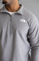 A close-up of a man wearing a light gray heathered quarter-zip pullover from The North Face, featuring a white embroidered logo on the left chest.