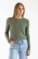 A woman wearing a fitted long-sleeve crewneck top in olive green, paired with light-wash blue jeans, photographed against a plain white studio background.