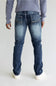 Rear view of a person wearing blue denim jeans with a light gray ribbed sweater and white sneakers against a plain light gray studio background.