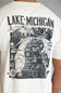 A close-up of a person wearing a cream-colored t-shirt, showing the back of the shirt with a large black graphic map of Lake Michigan and surrounding counties.