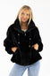 A woman wearing a black faux fur hooded jacket with a drawstring and zipper, paired with light blue jeans, against a plain white background.