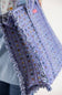 A close-up of a person holding a lavender patterned quilted bag with black and white striped ruffle trim.