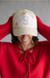 Woman wearing a beige cap with 'USA' and red sweater against a gray background