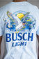 A man wearing a light blue crewneck t-shirt with a large graphic on the back. The graphic features the words 'BUSCH LIGHT' in blue, a white goose with yellow wings, and a yellow sun over blue waves.