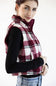 A woman wearing a burgundy, white, and gray plaid zip-up fleece vest over a black long-sleeve shirt and blue jeans, photographed against a plain white background.