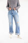 A person wearing cuffed light-wash blue distressed jeans with a striped long-sleeve top and white slip-on shoes, standing against a plain white studio background.