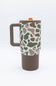 A travel mug with a brown handle and base, featuring a beige upper body covered in a green and brown camouflage pattern. It has a matching brown lid with a small orange accent tab.