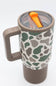 A travel tumbler with a handle, featuring a green and gray camouflage pattern on a white background, with a brown lid and handle, and an orange straw visible inside.