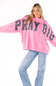 A woman modeling a bright pink sweatshirt with 'PRAY BIG' written across the front in large black letters filled with a floral pattern, paired with light blue jeans against a plain white background.