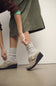 A person wearing taupe wedge clogs with buckle straps and light gray heathered crew socks, shown from the waist down in an indoor setting.