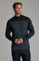A man wearing a dark charcoal and black quarter-zip long-sleeve athletic shirt, paired with dark jeans, standing against a solid gray studio background.