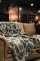 A cozy brown leather sofa in a dimly lit room, draped with a plush throw blanket featuring a gray, beige, and brown organic spot pattern.