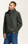 A man wearing a dark gray quarter-zip fleece pullover sweater and blue jeans, standing against a plain off-white studio background.